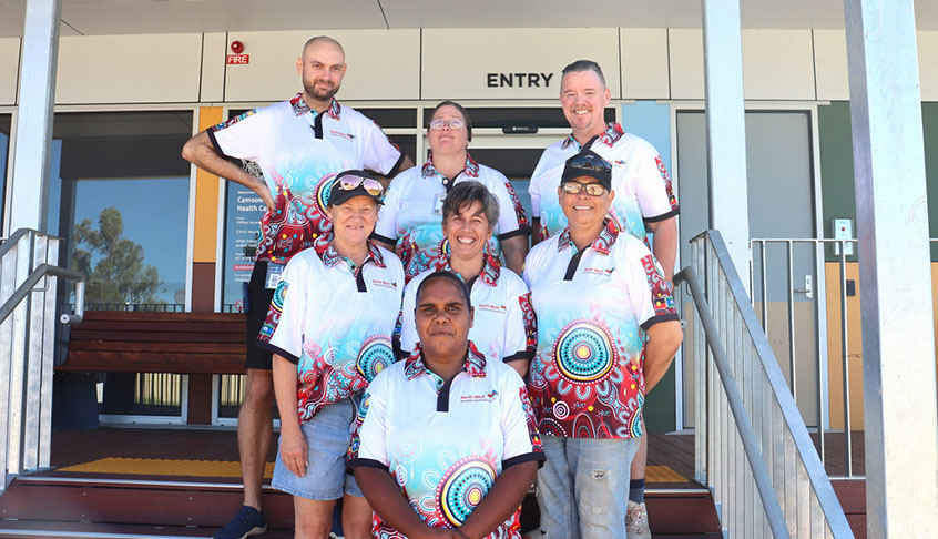 A group of people in matching shirts stands together on a set of steps, smiling and posing for the photo.