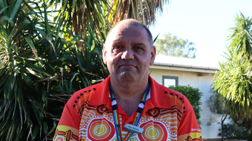 A man wearing a vibrant, colorful shirt stands confidently, showcasing a mix of bright patterns and hues.