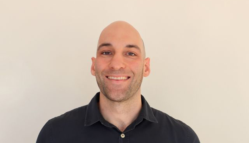 A bald man wearing a black shirt smiles warmly at the camera.