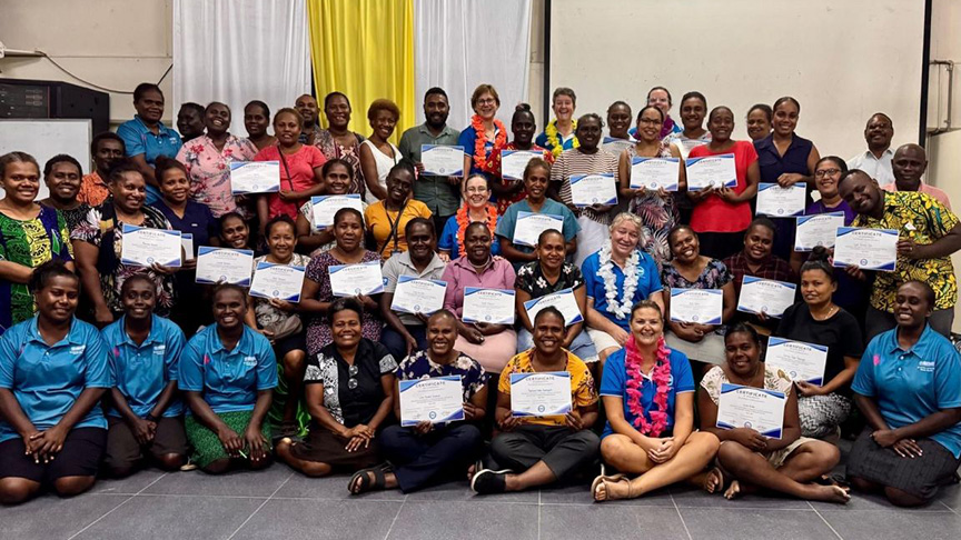 A group of women proudly display their certificates in front of a large audience at a formal event.