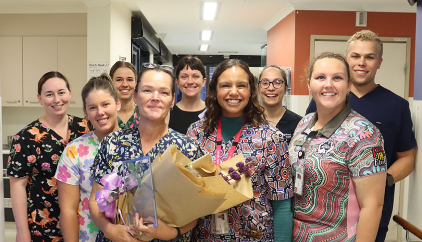 A group of nurses stands in a hallway, smiling and holding colorful flowers, showcasing teamwork and care.