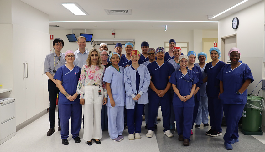 A group of people in scrub suits smiling and posing together for a photo in a well-lit environment.