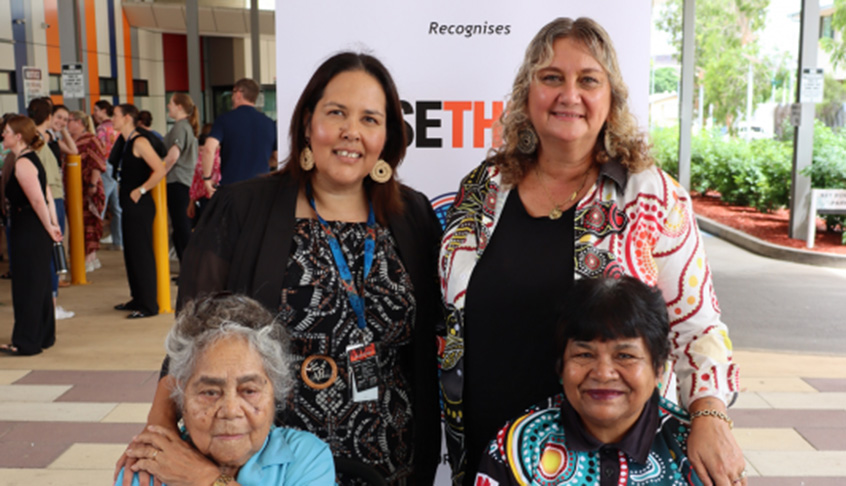 Four individuals, three women and one man, pose together for a photo at a social event.