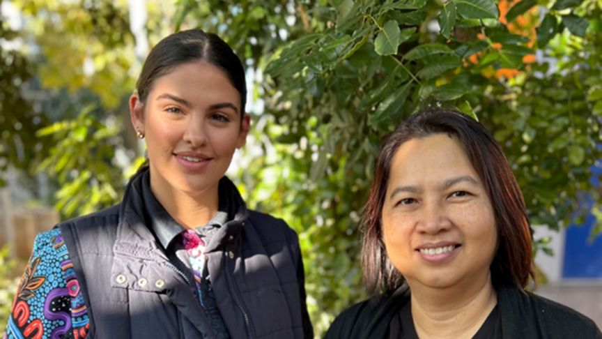 Two women pose together with trees in the background, showcasing a natural setting.