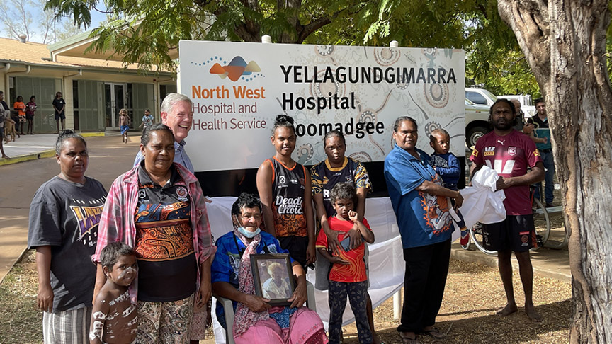 A group of people stands in front of a sign reading 'Yellagundgimarra Hospital', smiling and engaged in conversation.