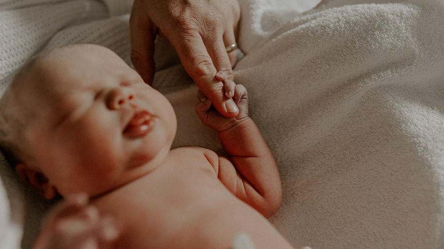 A person gently holds a newborn baby, showcasing a tender moment of care and connection.