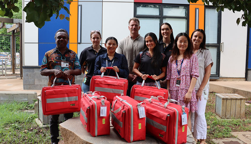 A group of diverse individuals smiling and posing together, each holding a red bag.