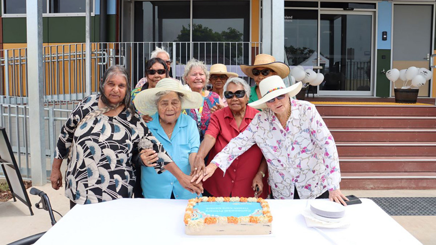 A group of women gathered around a decorated cake, smiling and celebrating together.
